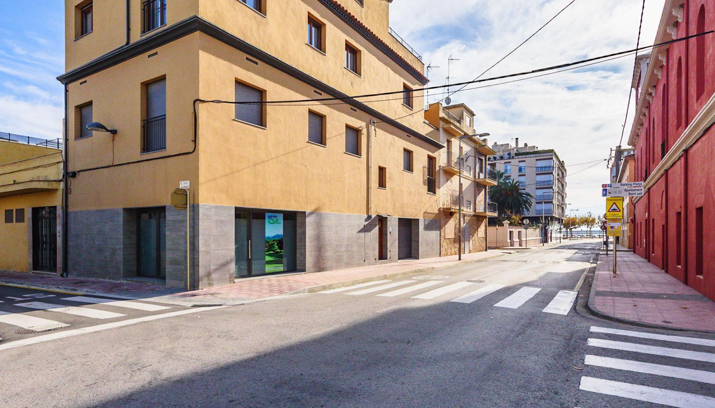 A multi-story building with a beige facade, a visible entrance, and a crosswalk in front.