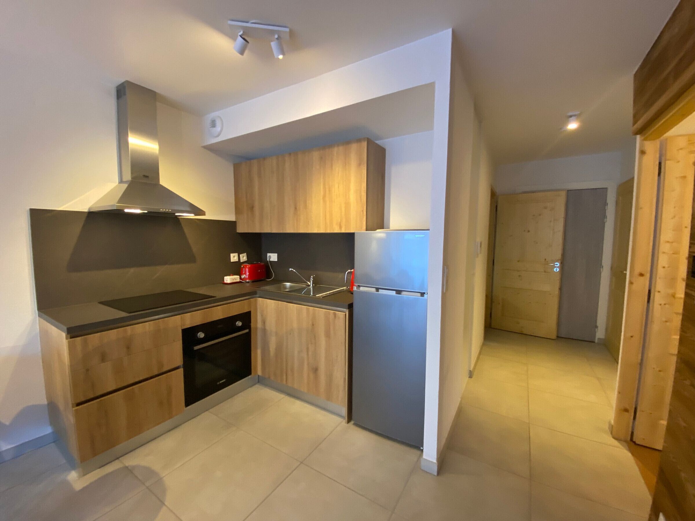 A modern kitchen with wooden cabinets, a stainless steel range hood, a built-in oven, and a refrigerator.