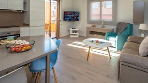 Ein modernes Apartment mit Küche, Essbereich und Wohnzimmer. Ein Fernseher ist an der Wand befestigt, es gibt ein Sofa und einen Couchtisch.