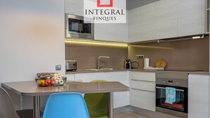 Eine moderne Küche mit integriertem Mikrowellenherd, Toaster und Backofen. Ein Esstisch mit Stühlen und eine Schüssel Obst sind ebenfalls vorhanden.