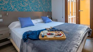 Ein ordentlich bezogenes Bett mit blauen Kissen, ein Tablett mit Frühstücksangeboten und eine Wand mit Muster im Hintergrund.