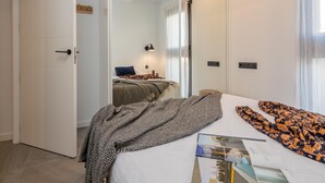 A bedroom with a bed, a bedside table, a lamp, and a door leading to another room. - Modern Penthouse with Terrace & AC - Palamós (Palamós)
