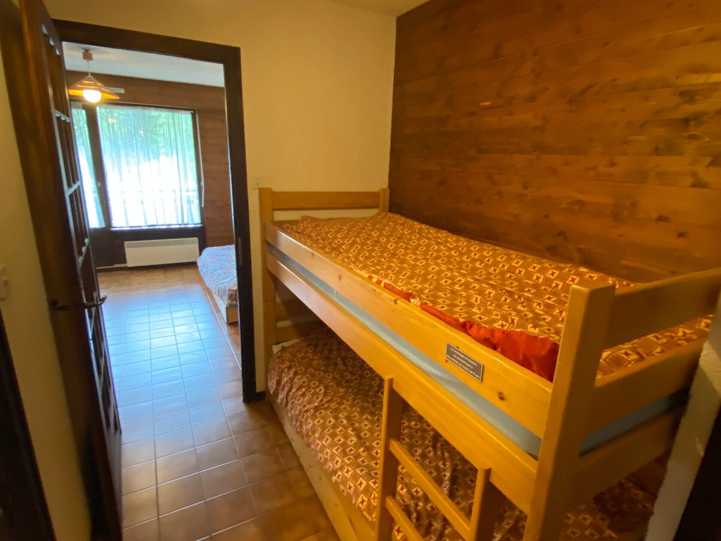 A bunk bed room with a wooden headboard, a window with blinds, and a tiled floor.