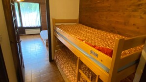 Habitació amb lliteres, un capçal de llit de fusta, una finestra amb persianes i un paviment de rajoles.
