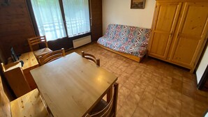Una zona de menjador amb taula i cadires de fusta, un sofà amb funda estampada i un armari de fusta.