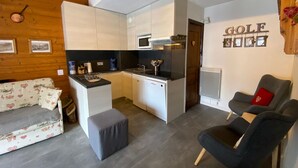 Un espacio habitable pequeño con kitchenette, un sofá estampado con motivos florales y una pared con un cartel de 'GOLF'.