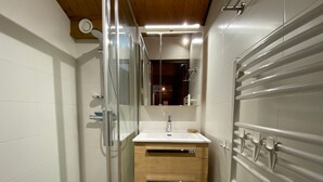 Un baño moderno con cabina de ducha de vidrio, tocador de madera con espejo y pared con azulejos blancos.