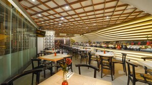 A modern restaurant with a high ceiling and wooden beams, featuring multiple tables and chairs. - Brits Hotel Legian (Kuta)