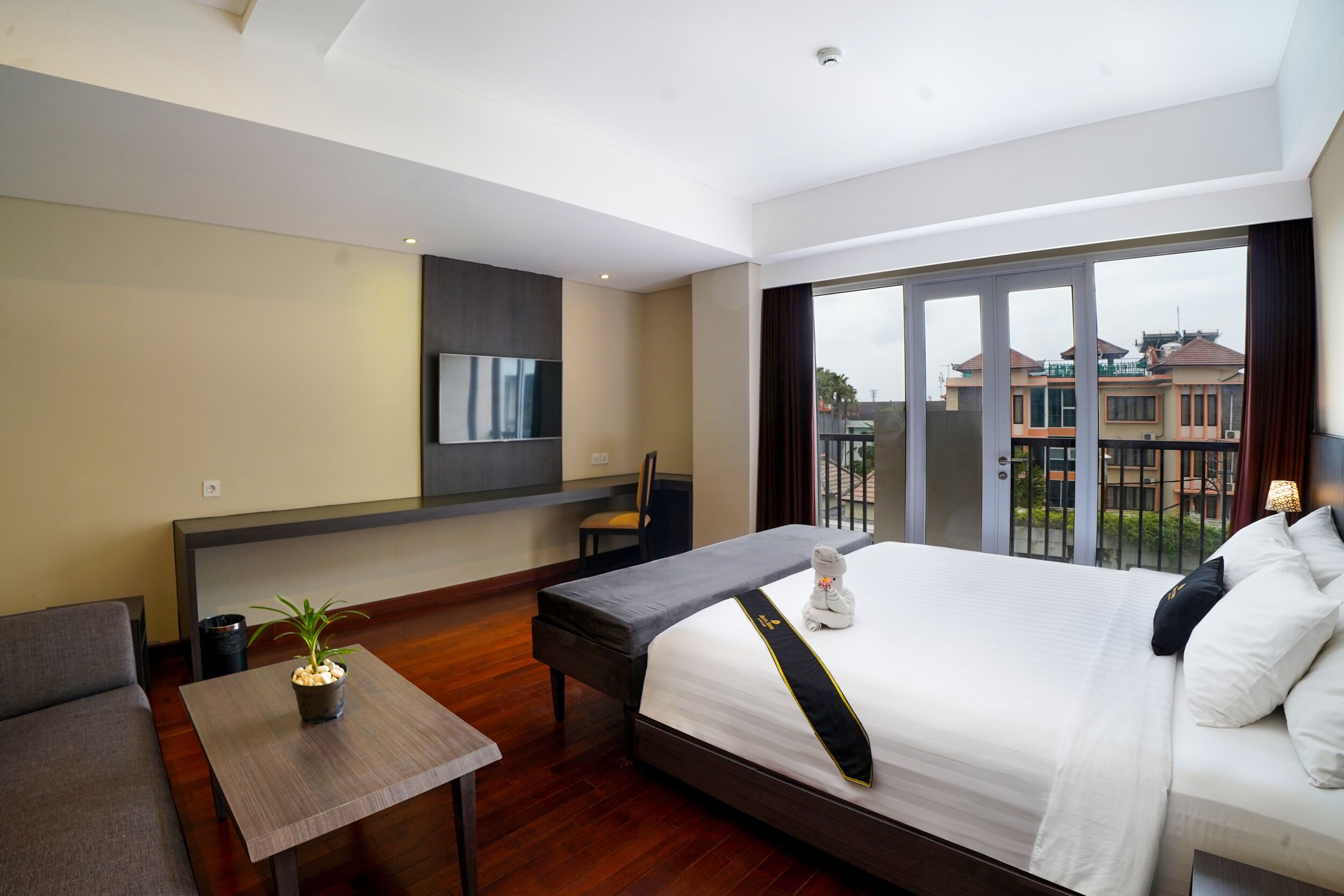 Una habitación de hotel moderna con una cama grande, una mesita con una planta, un sofá y un balcón con vistas a edificios.