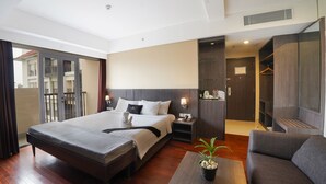 A modern hotel room with a large bed, a sofa, a bedside table with a plant, and a wardrobe. - Brits Hotel Legian (Kuta)
