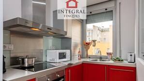 A modern kitchen with red cabinets, a stainless steel range hood, a microwave, a stove, and a window with a view of buildings. - Duplex Cosy avec Grande Terrasse à 50m de la Plage de Palamós (Palamós)