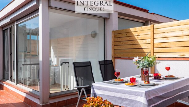 A dining area with a table set for two, a wooden fence, and a sign reading "INTEGRAL FINQUES". - Duplex Cosy avec Grande Terrasse à 50m de la Plage de Palamós (Palamós)