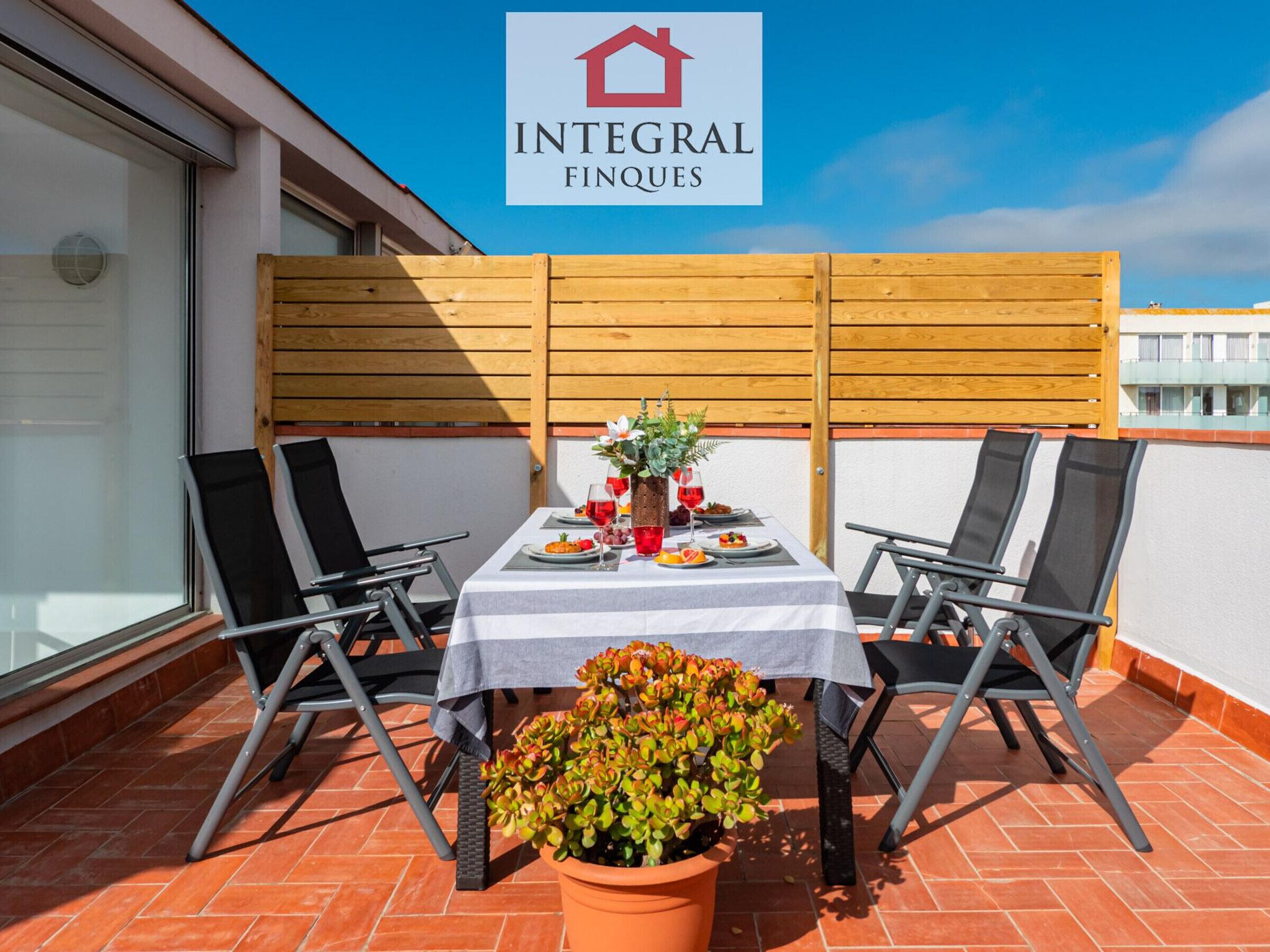 A terrace with a table set for two, two chairs, and a potted plant.
