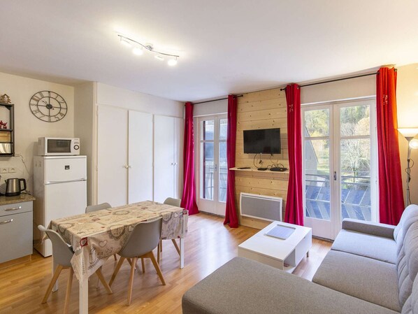 A modern living room with a dining table, sofa, TV, and kitchen area with a microwave and refrigerator.