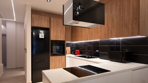 Eine moderne Küche mit eingebautem Backofen, einem schwarzen Kühlschrank, einer Kaffeemaschine und einer schwarzen Induktionskochplatte.