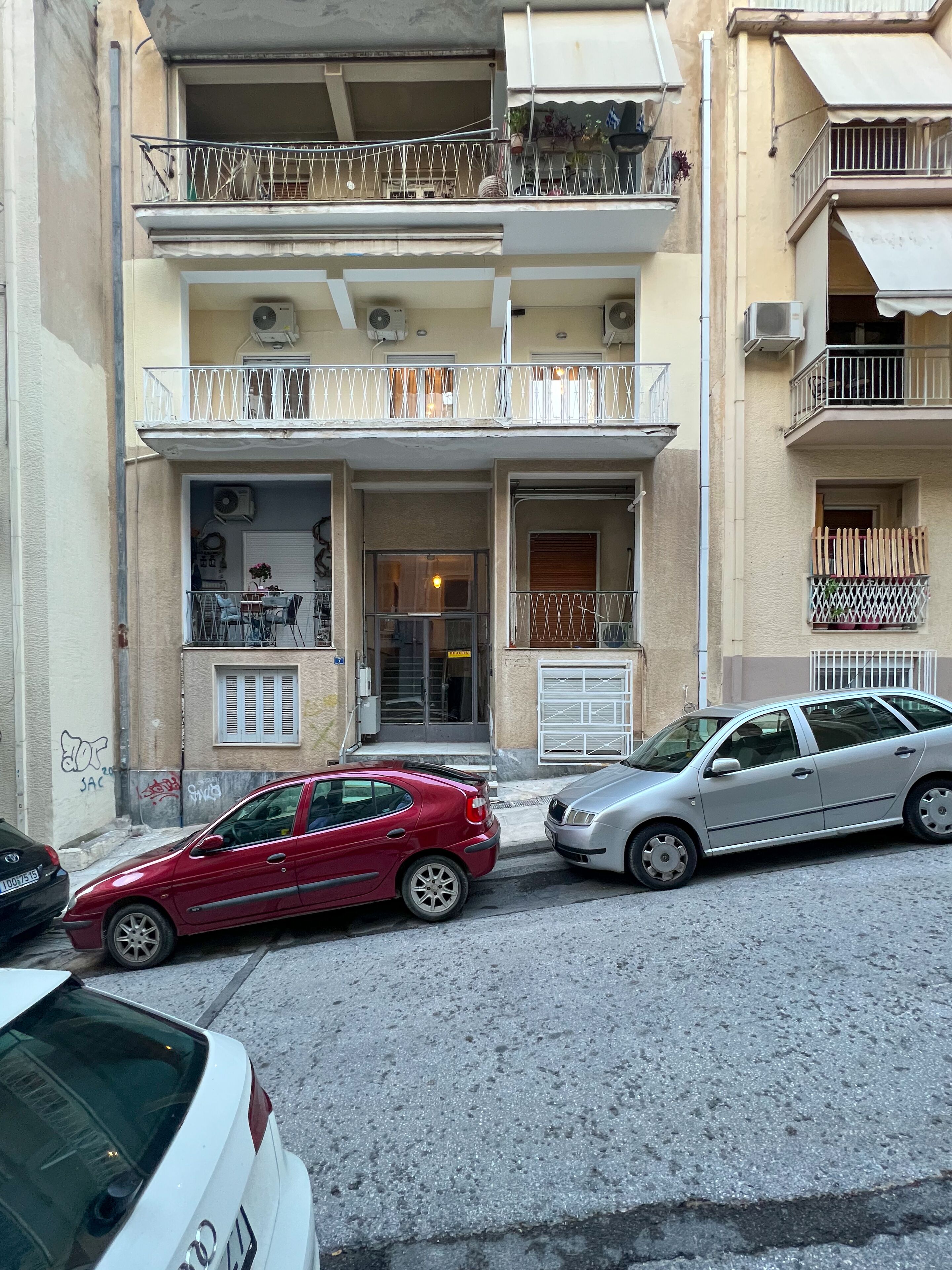 A building with a ground-floor entrance, a balcony with a metal railing, and a car parked in front.
