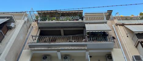 A multi-story residential building with balconies, air conditioning units, and a clear blue sky.