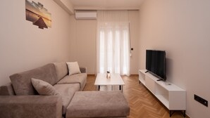 Ein modernes Wohnzimmer mit Sofa, Hocker, Fernseher und Couchtisch.
