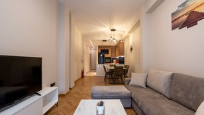 Ein modernes Wohnzimmer mit einem Flachbildfernseher, einem grauen Sofa, einem weißen Couchtisch und einem Holzboden mit Fischgrätmuster.