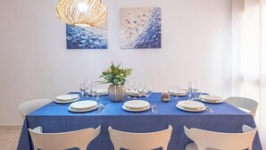 Ein Essbereich mit blauer Tischdecke, weißen Stühlen und einer Blumenvase.