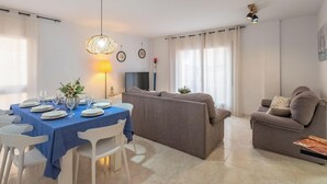 Ein modernes Wohnzimmer mit Essbereich, grauen Sofas, einem Flachbildfernseher und einem Esstisch, gedeckt für sechs Personen.