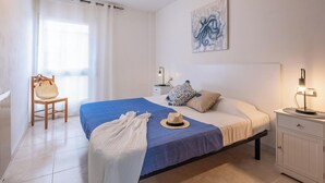 Ein Schlafzimmer mit Bett, Stuhl, Nachttisch und Wandbild.