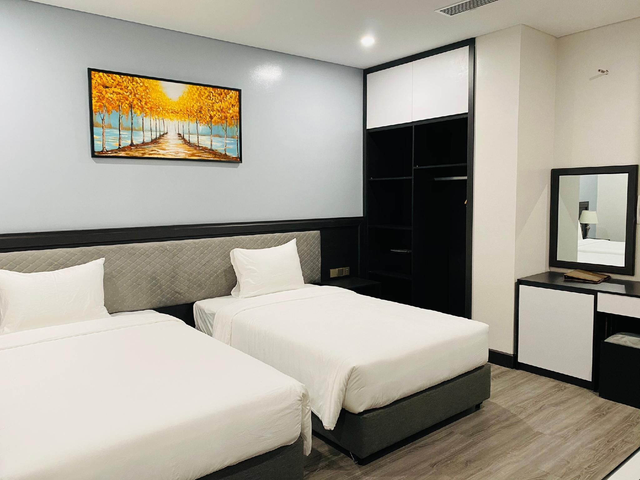 A hotel room with two beds, a wardrobe, a desk with a mirror, and a painting on the wall.