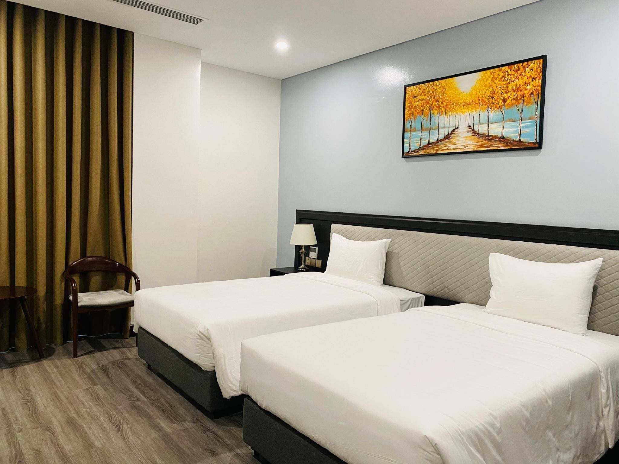 Habitación de hotel con dos camas, una mesita de noche con lámpara, una silla y un cuadro en la pared.