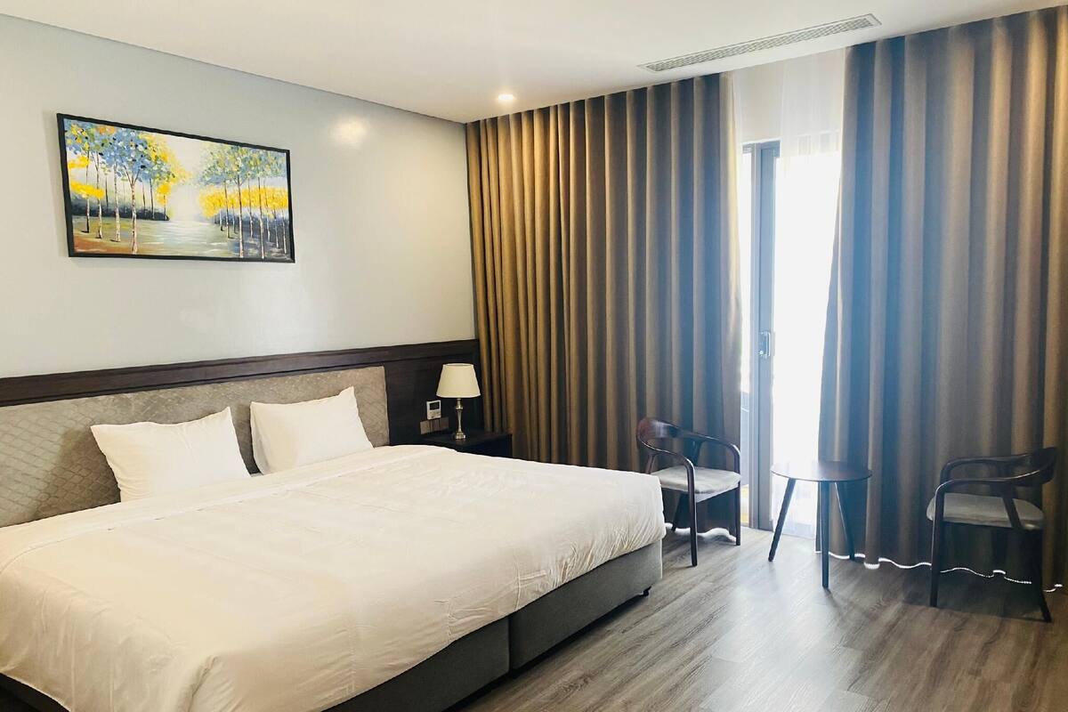 Habitación de hotel con una cama grande, una mesita de noche con lámpara, una silla y un cuadro en la pared.