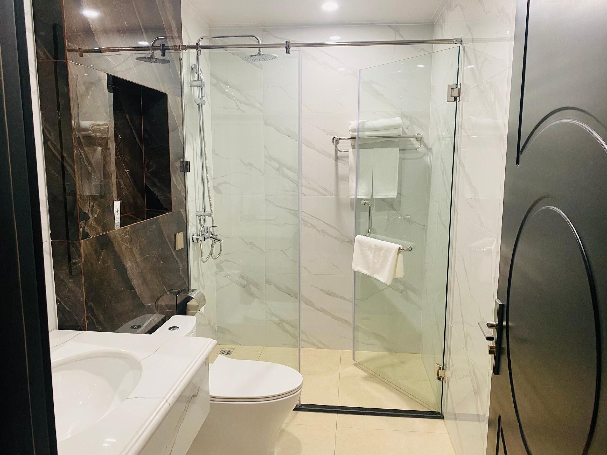 A modern bathroom with a glass-enclosed shower, a white toilet, and a marble-tiled vanity.