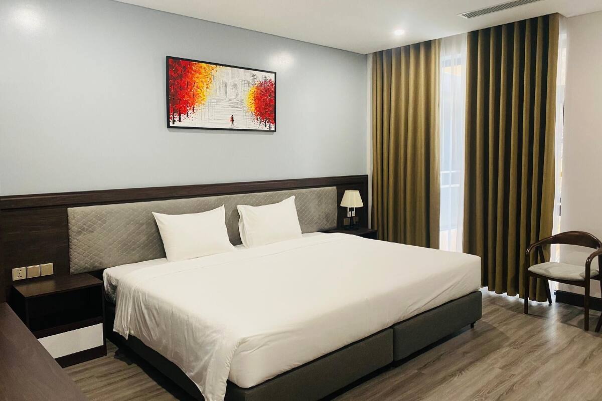 Una habitación de hotel con una cama grande, una mesita de noche, una lámpara y una silla.