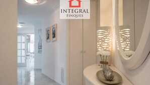 A hallway with a white door, a decorative wall panel, and a mirror reflecting a white flower arrangement.