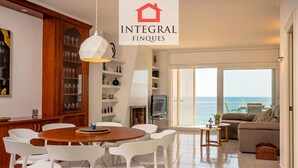 A modern living room with a dining area, a fireplace, and a large window overlooking the sea.