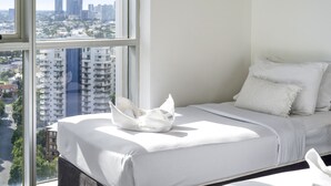 Une chambre d’hôtel dotée d’une grande fenêtre donnant sur la ville, un lit soigneusement fait avec du linge de lit blanc, et une vue sur le paysage urbain visible à travers la fenêtre.