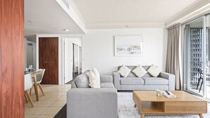 Un salon moderne avec un canapé gris, une table basse en bois et un coin repas comprenant une table et des chaises blanches.