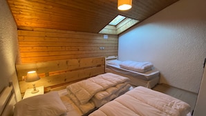 A room with two beds, wooden walls, a skylight, and a bedside lamp. - Bright apartment near Linga with WiFi and parking, South/East balcony (Châtel)