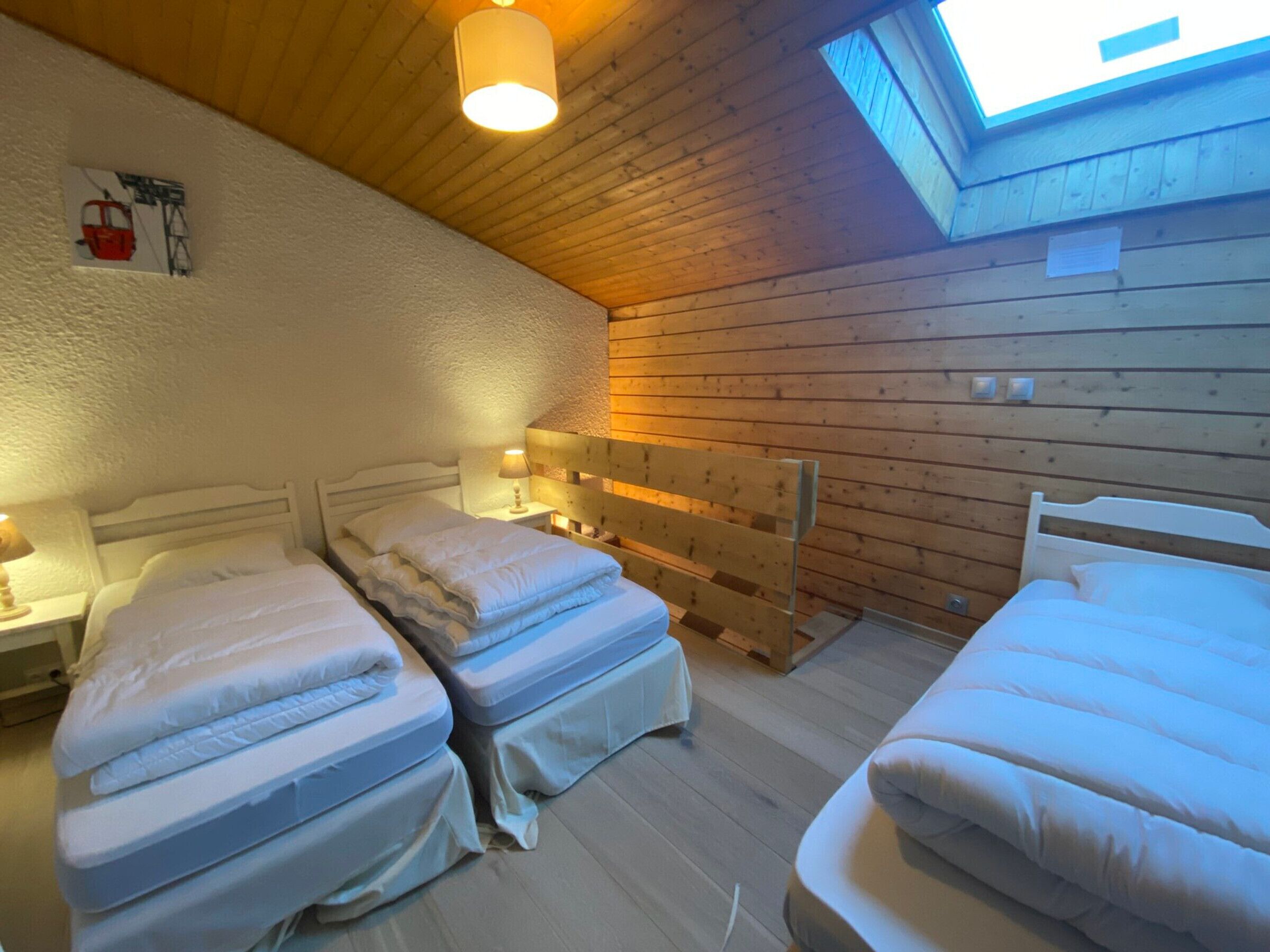 A room with two beds, a wooden headboard, a skylight, and a small table with a lamp.