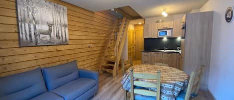 A wooden interior with a sofa, dining table, chairs, a kitchen area, and a staircase.