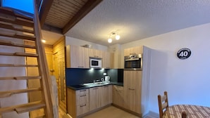A compact kitchen with wooden cabinets, a microwave, an oven, and a dining area with a table and chairs. - Bright apartment near Linga with WiFi and parking, South/East balcony (Châtel)
