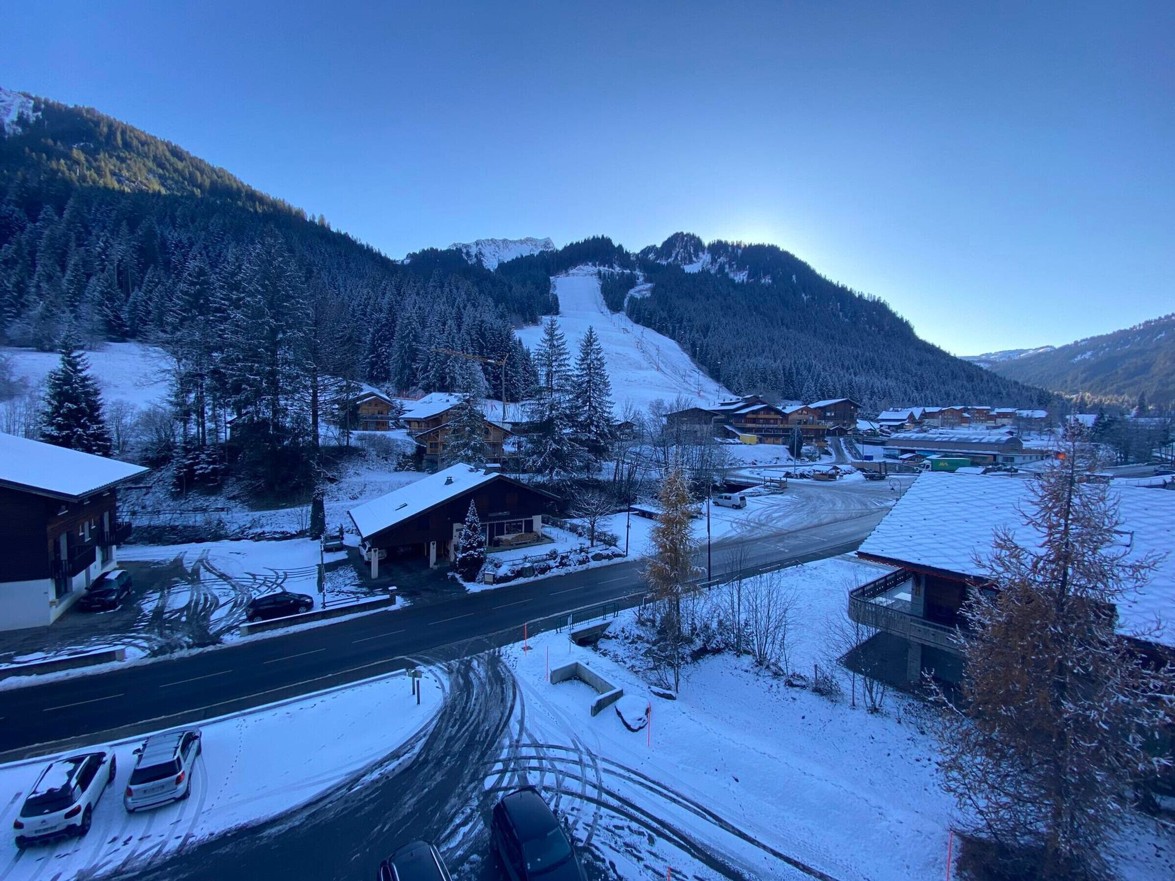 A snow-covered village with wooden buildings, a road, and a mountain in the background.