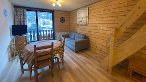 A wooden interior with a dining table, chairs, a sofa, a TV, and a staircase. - Bright apartment near Linga with WiFi and parking, South/East balcony (Châtel)
