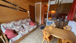 A cozy room with a wooden sofa, a wooden dining table, and chairs. There is a kitchen area with a sink and cabinets. - 18m² Studio near slopes, balcony, parking (La Chapelle-d'Abondance)