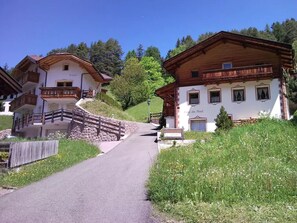 Un camino rural de montaña que lleva a casas de madera tradicionales con balcones y un puente de piedra.