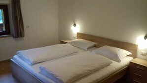 Ein Doppelbett mit weißer Bettwäsche, zwei Nachttische mit Lampen und ein Fenster mit Vorhängen.