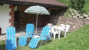 Eine Terrasse mit vier gestreiften Liegestühlen, einem Tisch, einem Sonnenschirm und einer Steinmauer.