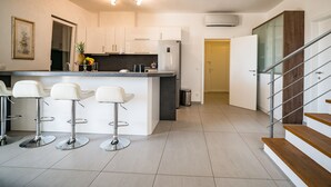 Una cucina moderna con mobili bianchi, un'isola centrale con sgabelli da bar e una scala che conduce a un livello superiore.