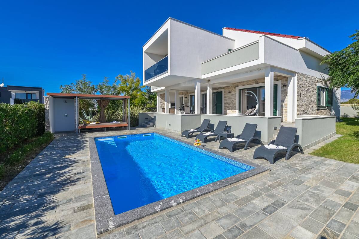 A modern two-story house with a swimming pool, outdoor seating, and a stone facade.
