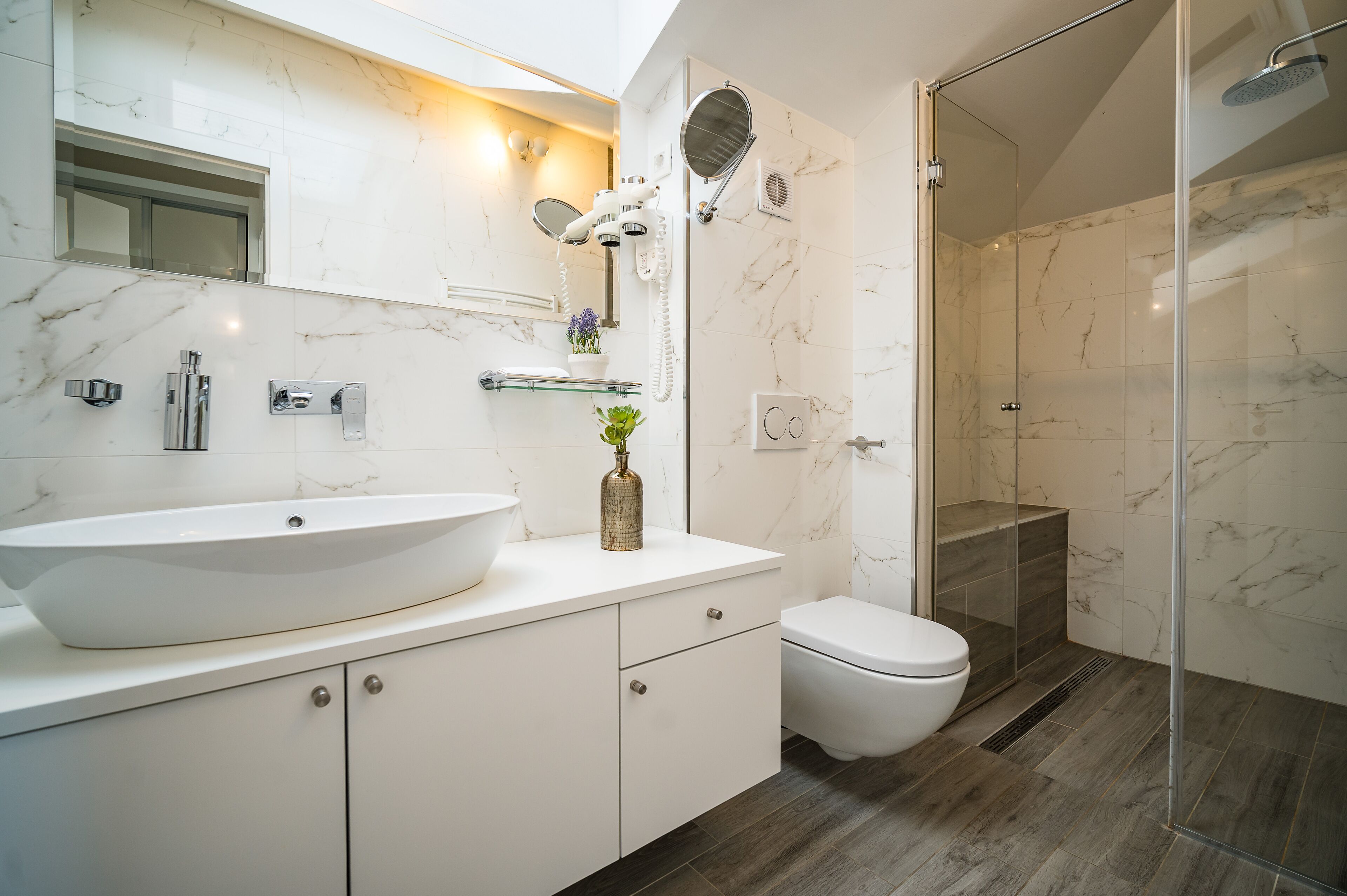 A modern bathroom with a large white sink, a toilet, and a glass-enclosed shower area.
