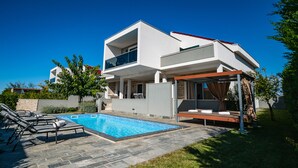 Una moderna casa a due piani con piscina, area salotto esterna e patio coperto.
