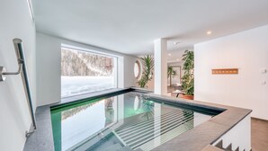A modern indoor pool with clear glass walls, a view of a snowy landscape, and minimalist decor.